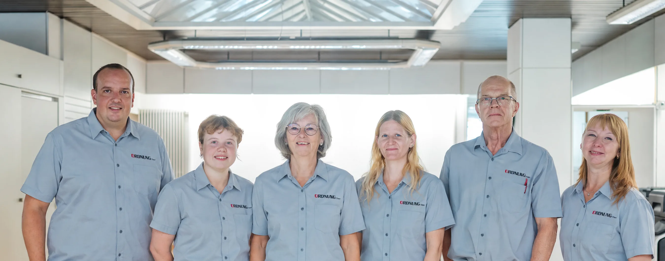 Das Team von Ordnung Trier in einheitlichen grauen Firmenhemden im Ausstellungsraum unter dem Glasdach